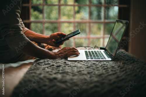 Man using phone and laptop on bed