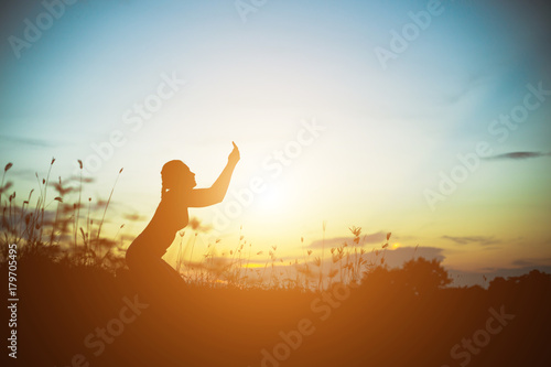 Silhouette of woman praying over beautiful sky background © Janpen