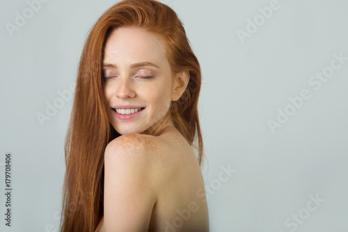 beautiful young girl with red hair with bare shoulders on a light background
