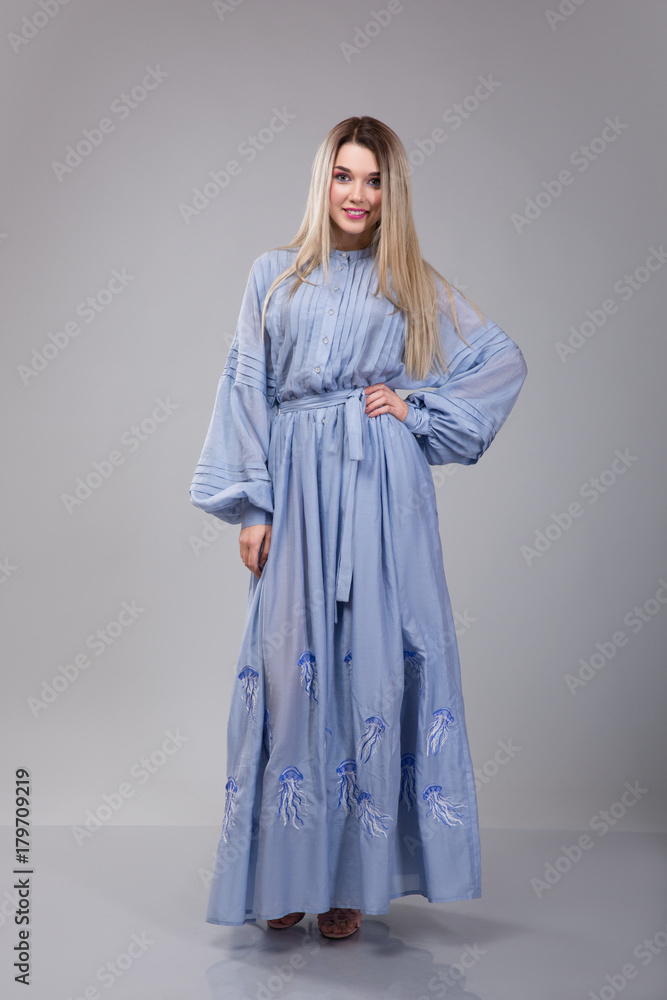 beautiful young woman dresseed in long blue embroidered dress on grey studio background beautiful young woman dresseed in long blue embroidered dress on grey studio background