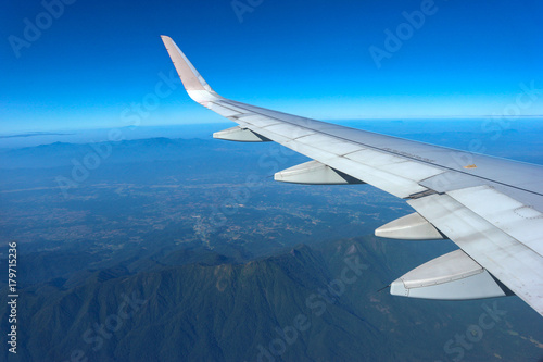 flying Airplane wing with blue sky and natural mountains at bottom