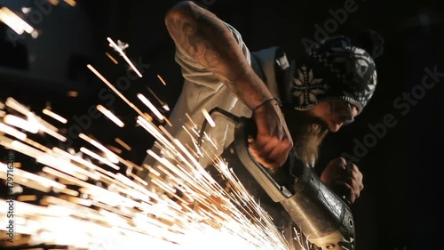 Bearded mechanic cuts metal with an angle grinder in a service station photo