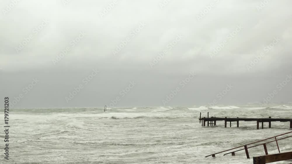 Old metal pier in the stormy sea and windsurfers in the open sea on the waves Old metal pier in the stormy sea and windsurfers in the open sea on the waves