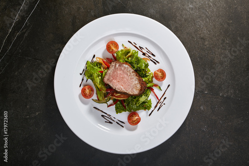 Roast beef with mixed salad and cherry tomatoes on black background