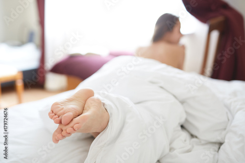 back view of young woman lies in bed early in the morning and with a satisfied smile stretches. focus on the feet