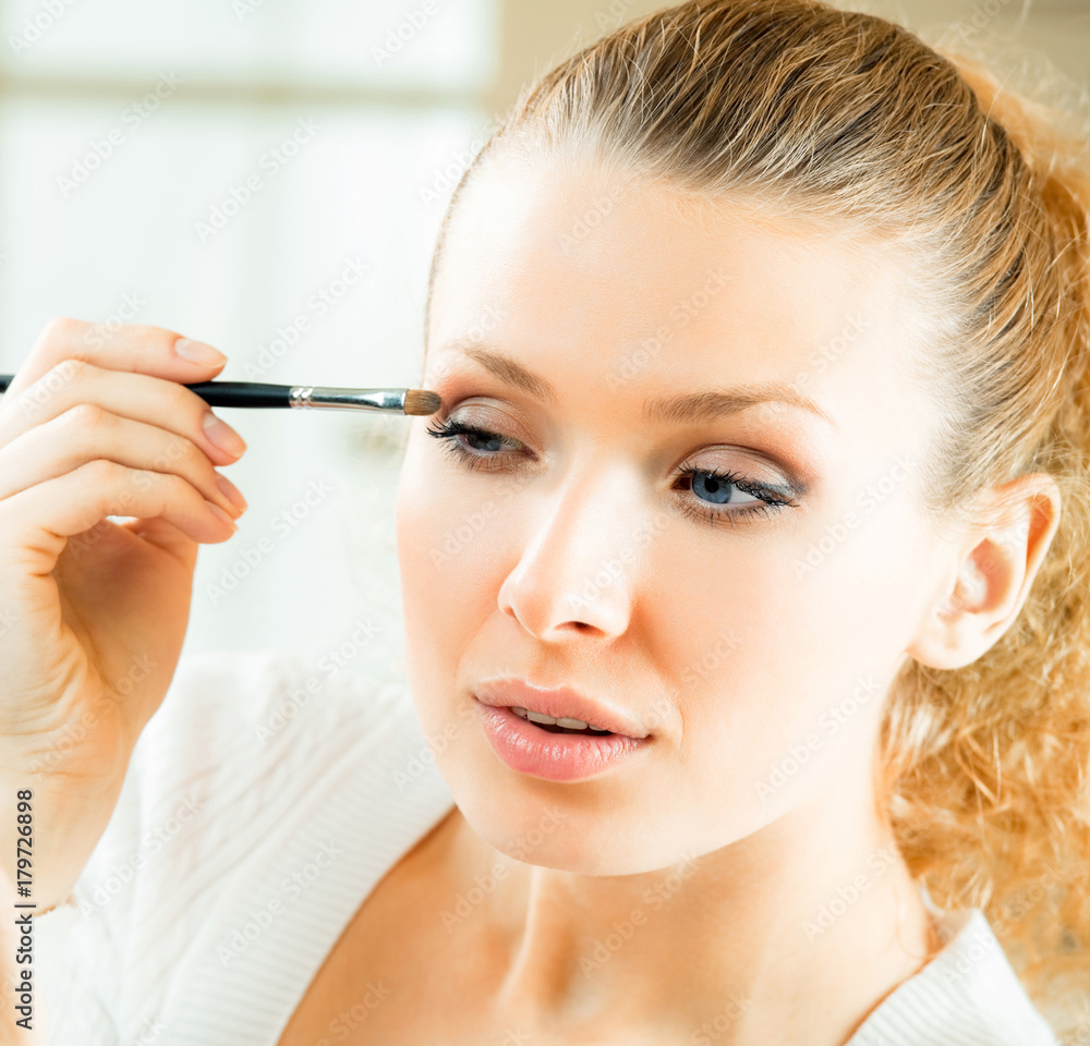 Cheerful smiling woman with mirror and makeup brush