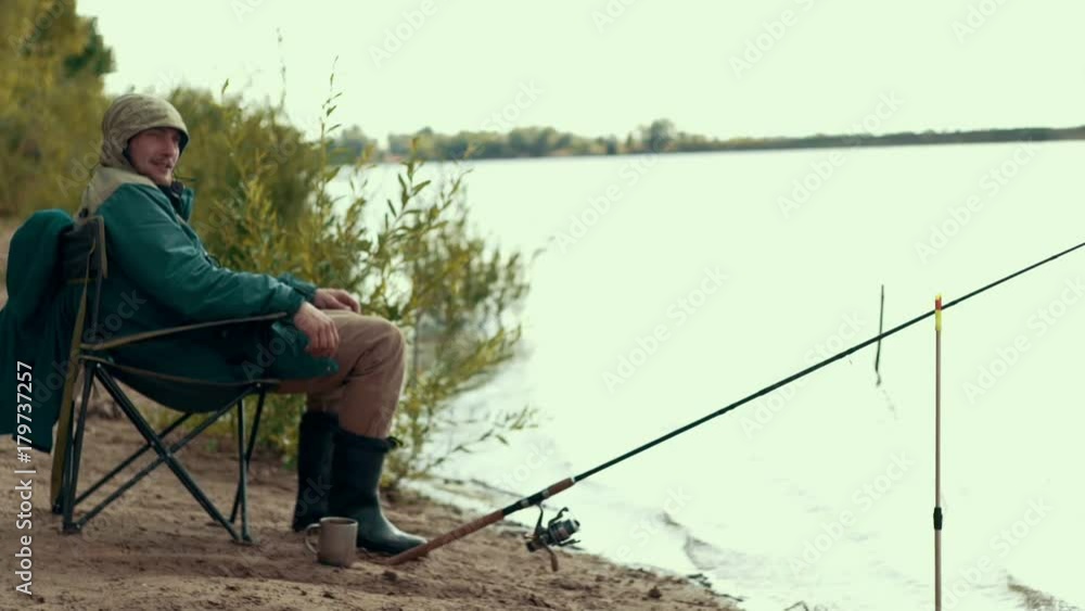Fisherman sitting on chair by river nearly fishing rod waiting for bite Fisherman sitting on chair by river nearly fishing rod waiting for bite