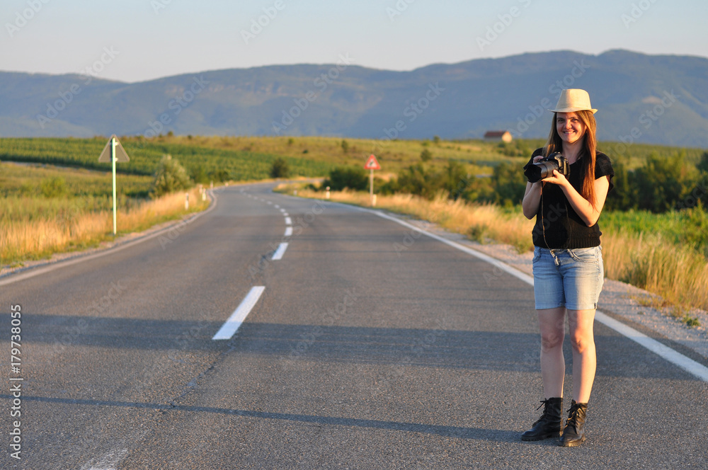 Woman walking with a camera on the middle of the road in mountains. Forty Years old (40 yo) woman on the road
