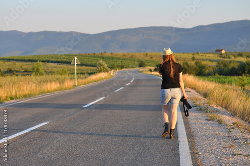 Woman walking with a camera on the middle of the road in mountains. Forty Years old (40 yo) woman on the road