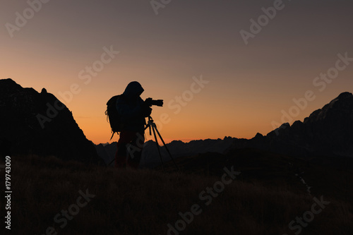 Photographer in the Dolomites taking pictures of sunset. Silhouette of a photographer on a golden background. Dolomites.