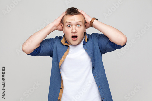 Young boy open mouth, holding head and looking at camera.