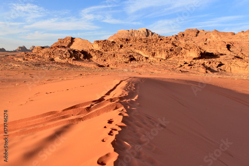 Wadi Rum desert in Jordan. Big area with smooth red dune and mountains at the background and blue sky with clouds.