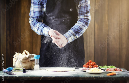 man in an apron preparing a pizza, knead the dough and puts ingr