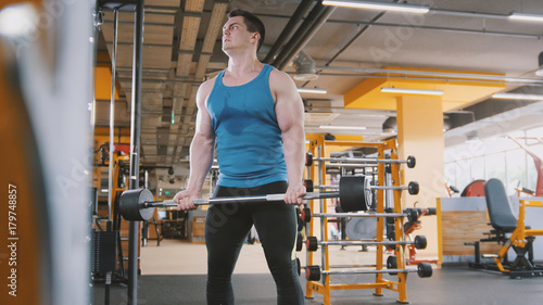 Bodybuilding in the gym - muscular man training his biceps near mirror