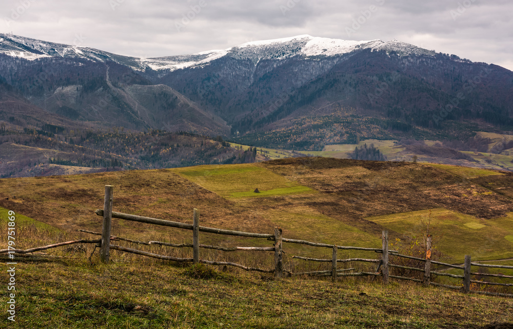 wooden fence on hills of mountainous countryside. agricultural fields in late autumn gloomy weather. mountain ridge with snowy tops in the distance