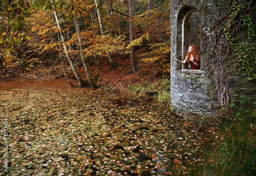 Pre- Raphaelite looking woman with long red hair posing wistfully in the open window of a Gothic tower photo