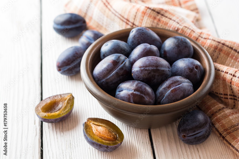 Fototapeta premium Fresh plums in ceramic bowl on white wooden background.