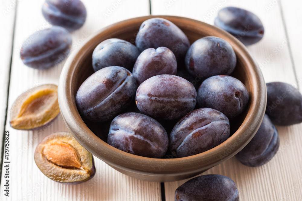 Obraz premium Fresh plums in ceramic bowl on white wooden background.