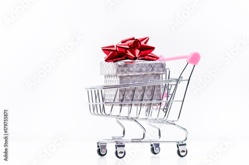 Shopping trolley with christmas gift. Gift box with red ribbon isolated on a white background. Christmas decoration. 