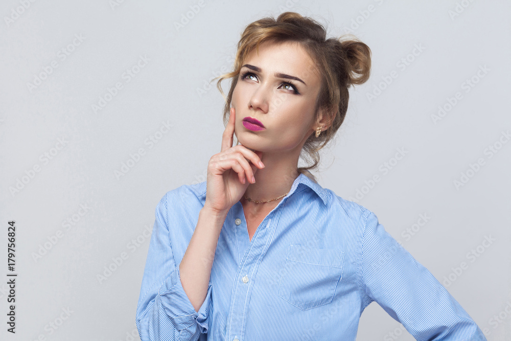 Indoor isolated studio shot on gray background of cute blonde girl looking away, having doubtful and indecisive face expression. Indoor isolated studio shot on gray background of cute blonde girl looking away, having doubtful and indecisive face expression.