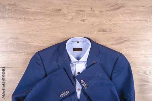 set of classic mens clothes - blue suit, shirts, brown shoes, belt and tie on wooden background.