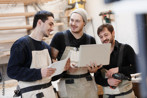 Master of small business with laptop and his team as sign of innovation in carpenter workshop. startup business, young specialist