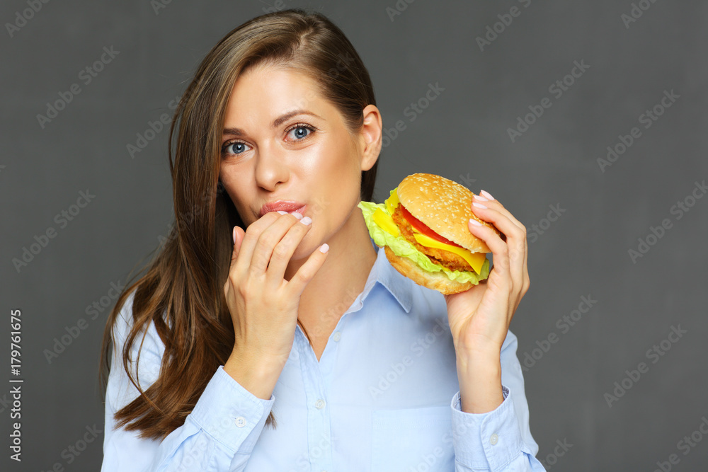 Smiling woman holding burger licks fingers.