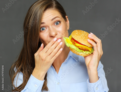 Smiling woman holding burger licks fingers.