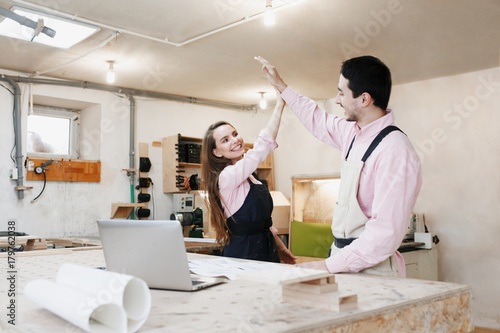 young happy family standing at a work bench in a carpentry workshop, writing a project. Family business. startup business. young specialist designer. photo