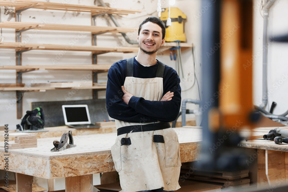 carpenter's portrait in work clothes in front of workbench. Portrait of smiling man at work in carpenter workshop. startup business, young specialist