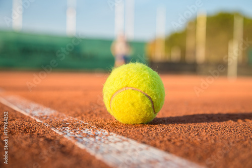Tennis ball lying on white line on tennis court on sunny day.  © pablobenii