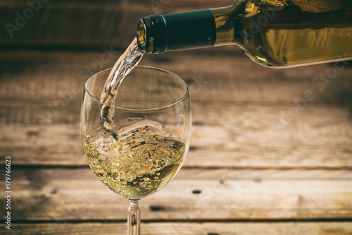 Pouring white wine in a glass on wooden background