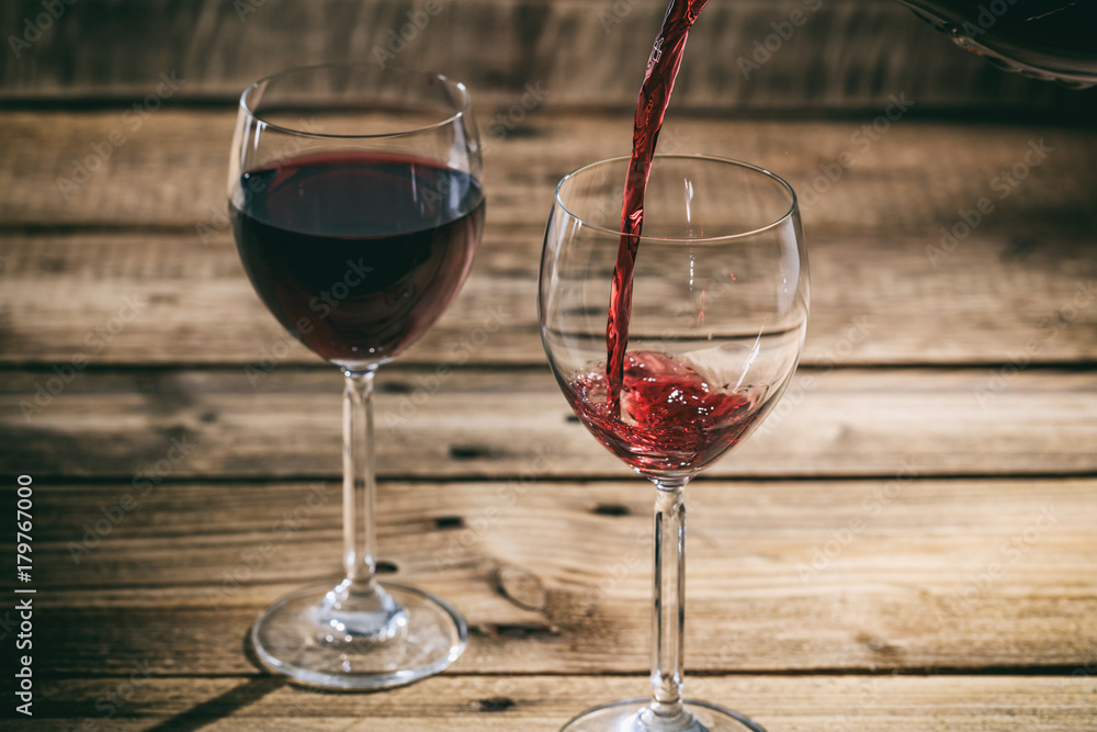 Pouring red wine in a glass on wooden background