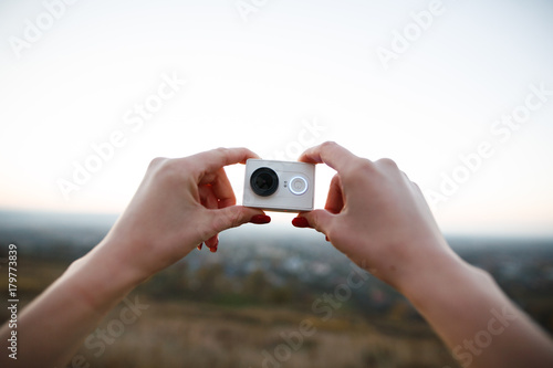 Man holds an action camera on the sunset background