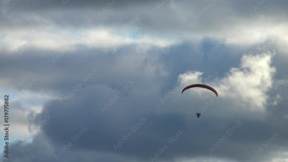 Paraglider flying high in the storm clouds. Air sport and recreation. A powered paraglider - a glider with a dorsal power plant, providing the rise and moving in the air. Paraglider flying high in the storm clouds. Air sport and recreation. A powered paraglider - a glider with a dorsal power plant, providing the rise and moving in the air.