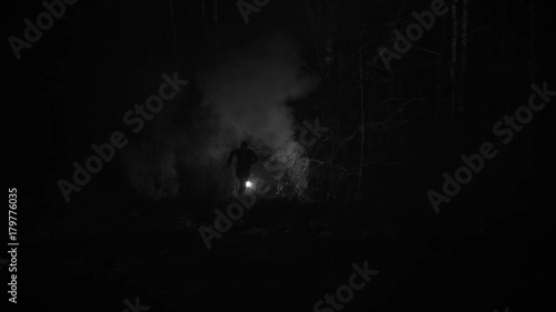 Silhouette of a man chased by light through the forest at winter night