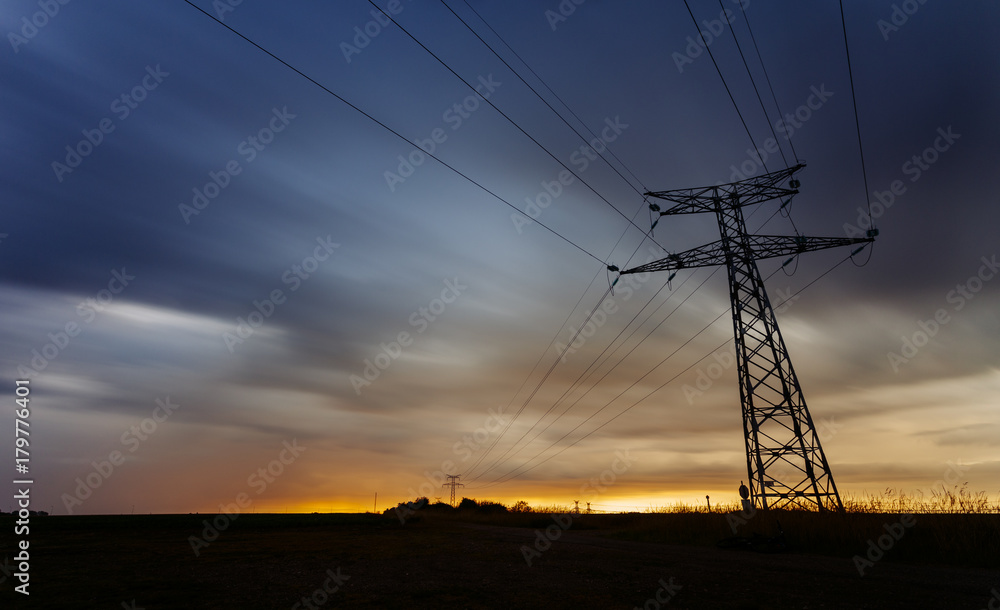 High voltage power lines and transmission towers at sunset. Pole and lines silhouettes in the dusk. Electricity generation and distribution. Electric power industry and nature concept. Long exposure
