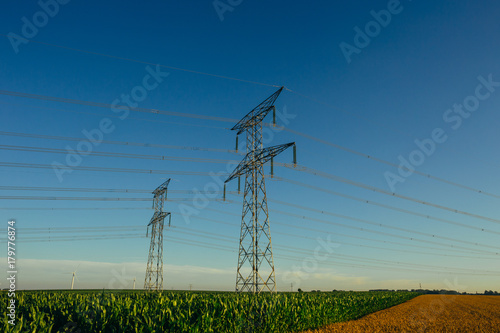 High voltage power lines and transmission towers in agricultural fields in Normandy, France. Electricity generation and distribution. Electric power industry, nature and agriculture concept
