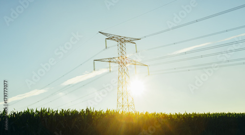 High voltage power lines and transmission towers with sunbeams in the blue sky in Normandy, France. Countryside landscape. Electricity generation and distribution. Electric power industry and nature