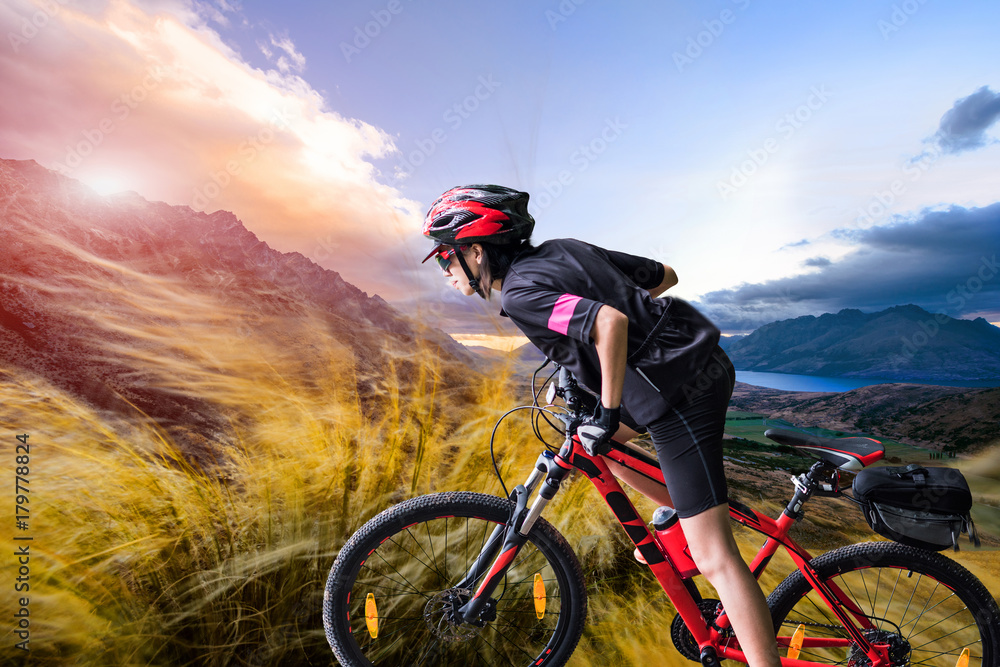 strong woman riding moutain bike upon the hill with strong windy impact through the on the moutain, river and moutain in background strong woman riding moutain bike upon the hill with strong windy impact through the on the moutain, river and moutain in background