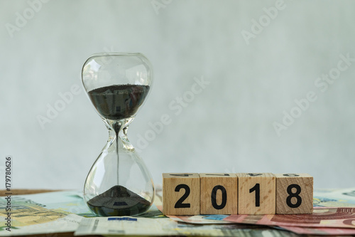 Year 2018 business time countdown or long term investment concept as hourglass or sandglass on pile of Euro banknotes with wooden cube block number 2018