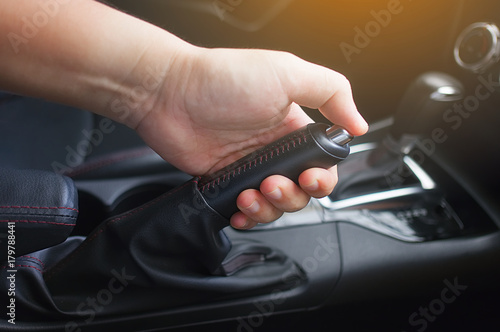Closeup of young man pulling handbrake lever in car