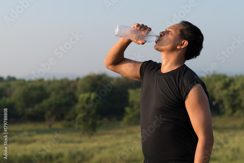 Young man drinking water after running exercise. in the background of blue sky © xreflex