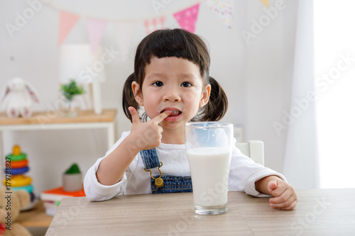 Adorable baby girl with dringking milk with milk mustache holding glass of milk