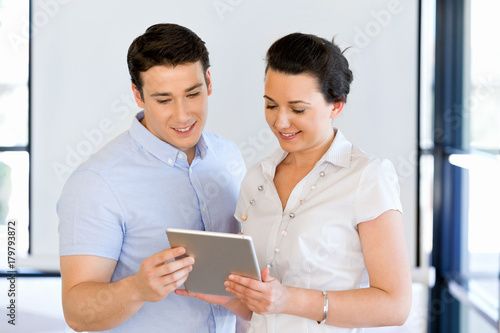 Young man and woman with touchpad standing in office