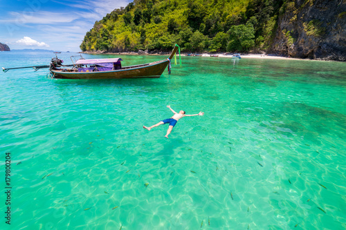 Young man traveler swimming surrounded by fish with long thai boat in Krabi Sea at Andaman Sea, Thailand