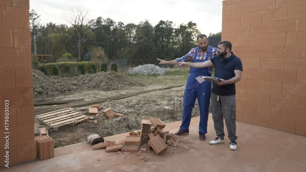 Male architect with blueprints talking to his worker about home project at construction site
Male architect with blueprints talking to his worker about home project at construction site