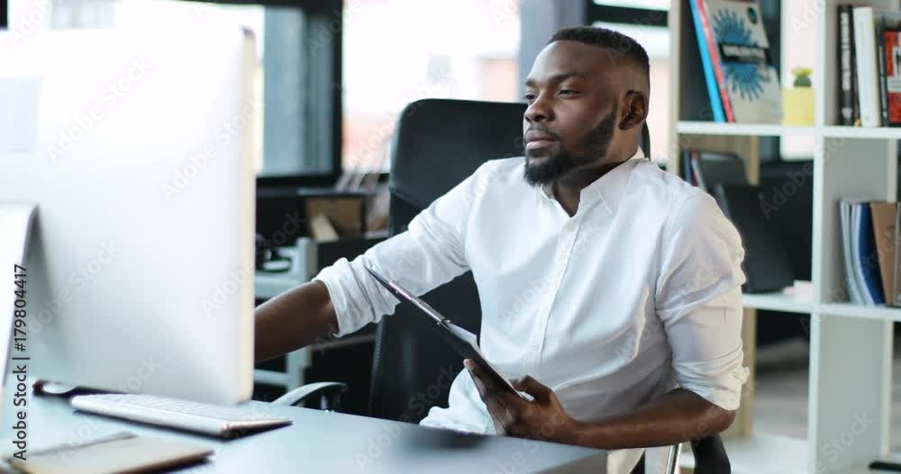 African American working in office using a computer writes documents focused on work looking in monitor screen technology businessman casual communication successful portrait business Slow Motion Shot