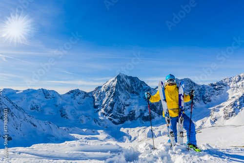 Mountaineer backcountry ski resting along a snowy ridge with skis in the backpack. In background blue sky and shiny sun and Ortler in South Tirol, Italy. Adventure winter extreme sport.