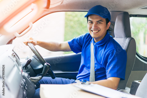 Young handsome delivery man driving his van with packages on the front seat